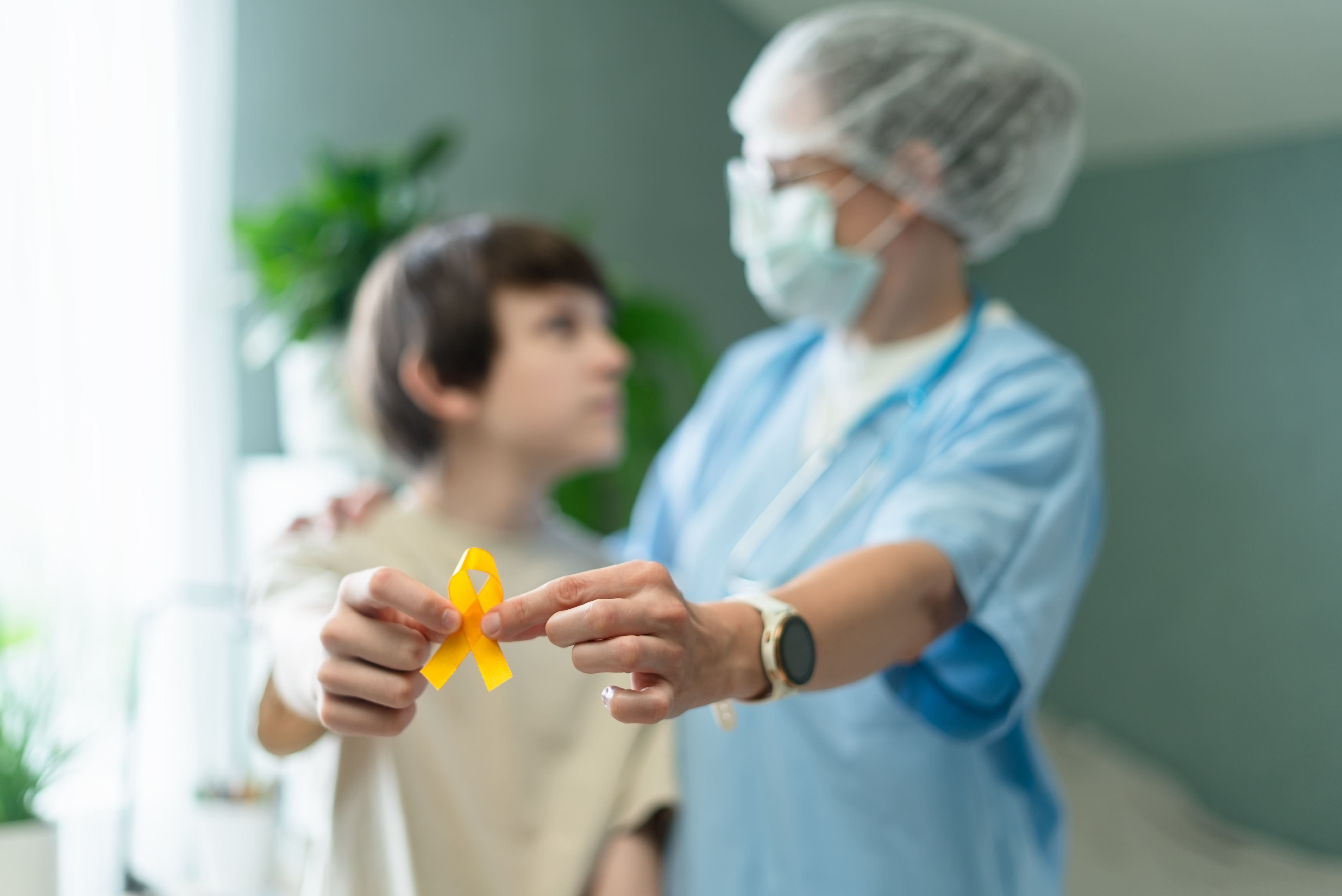 Compassionate nurse holding yellow ribbon to support childhood cancer awareness in hospital. Dedicated healthcare professional displays hope and care for patients.